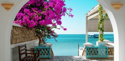 Beautiful Cycladic architecture frame with vibrant pink bougainvillea overlooking the turquoise Aegean sea.